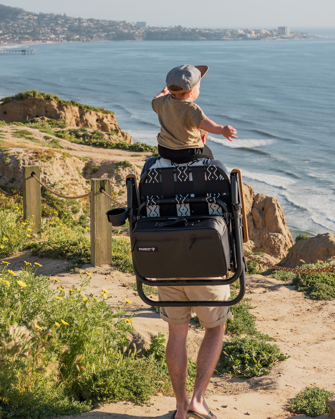 A child on a dads shoulders with a beach chair backpack