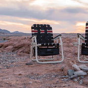 Foldable chair with a striped pattern in a desert landscape during sunset.